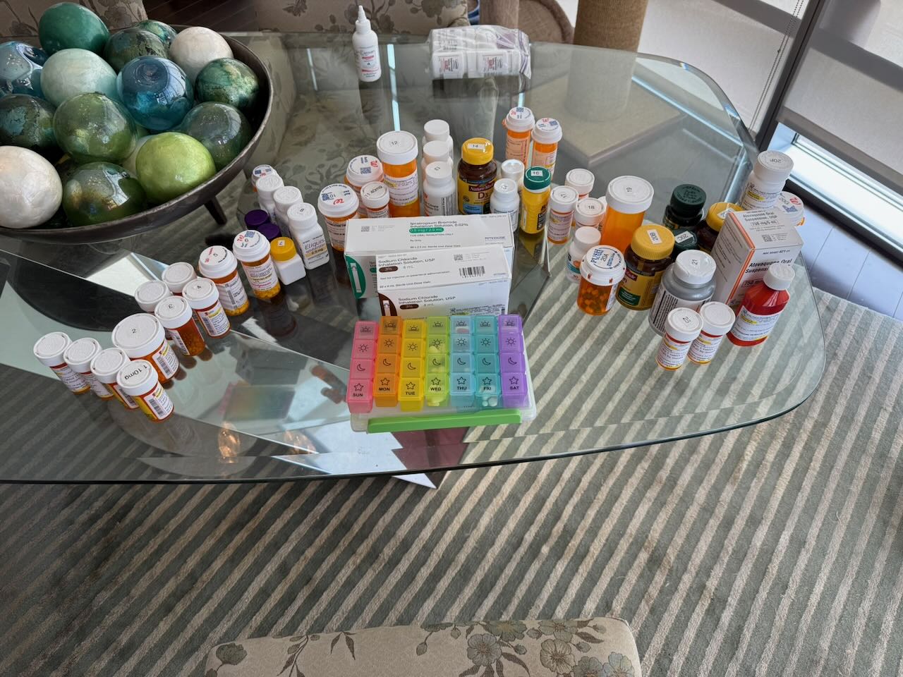 Lonna's full medication spread — every bottle numbered, rainbow pill organizer in the center